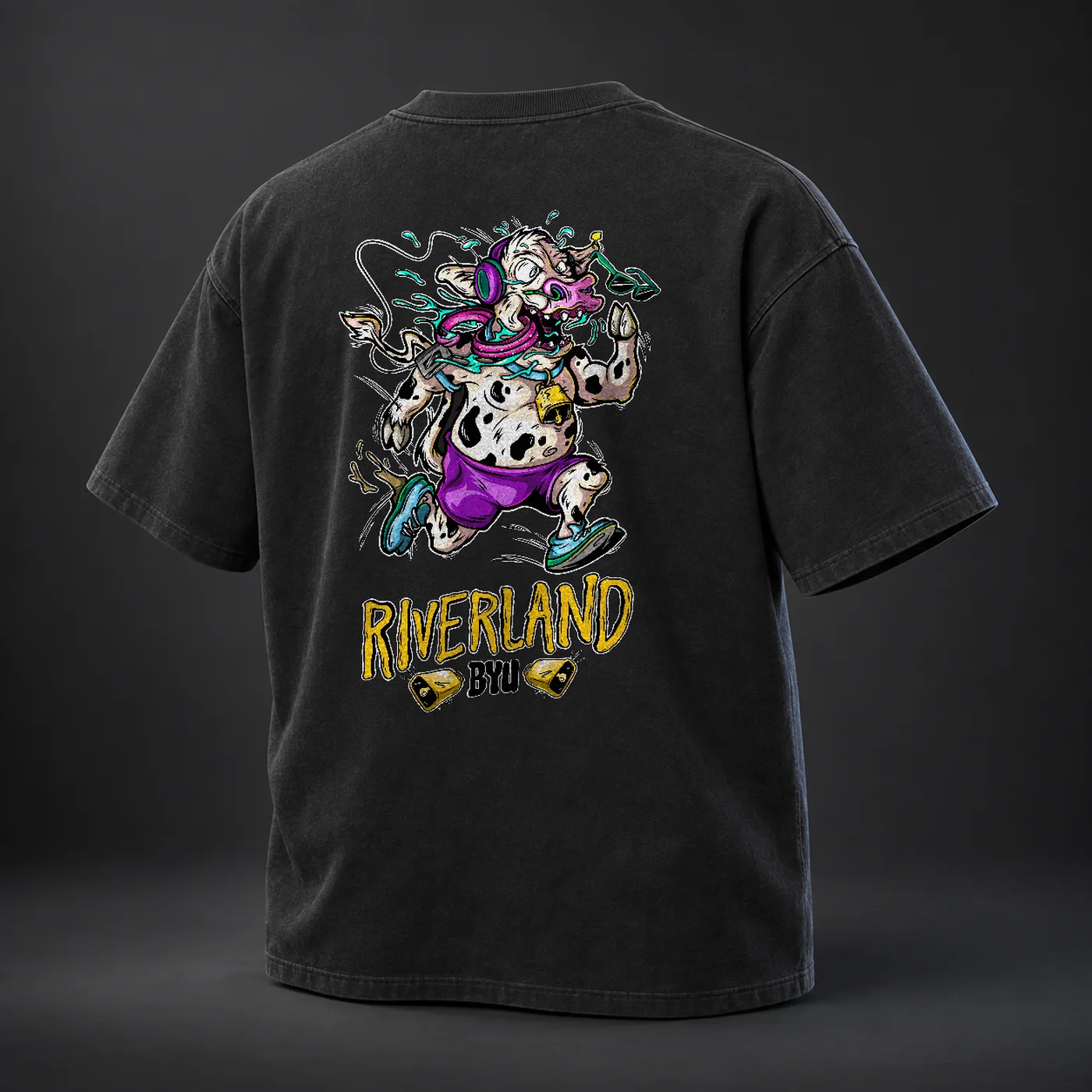 The faded black heavyweight tee seen from behind, printed with a colourful illustrated running cow above bold yellow RIVERLAND BYU lettering.
