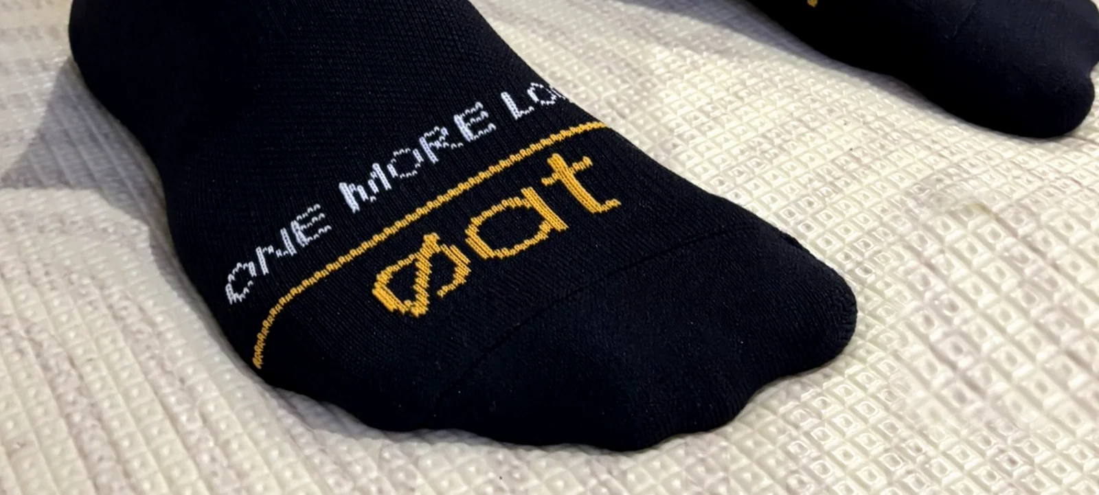 Detail of the forefoot of a worn sock, with ONE MORE LOOP curving in white above a gold line and the gold øat wordmark on the toe box.